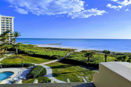 white concrete hotels and building near green field viewing calm sea under white and blue skies